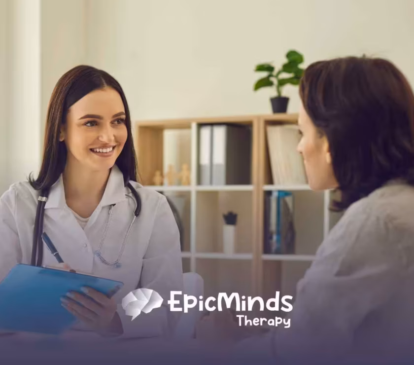 A smiling doctor with long dark hair holds a clipboard, attentively speaking to a patient in a well-lit office