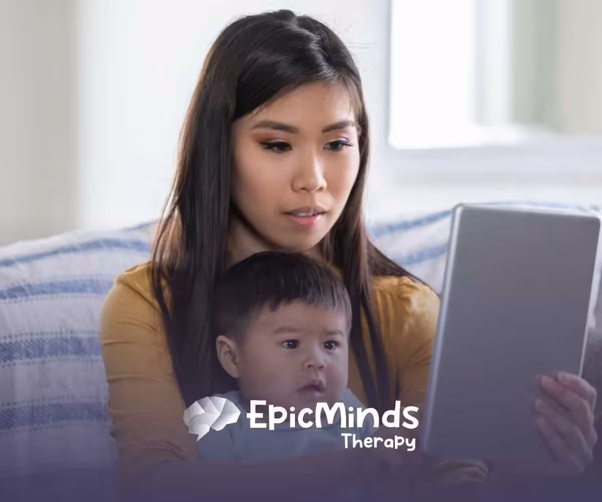 A woman and baby sit on a couch, engaged with a tablet. The woman looks focused, while the baby gazes at the screen. The setting is cozy and calm.
