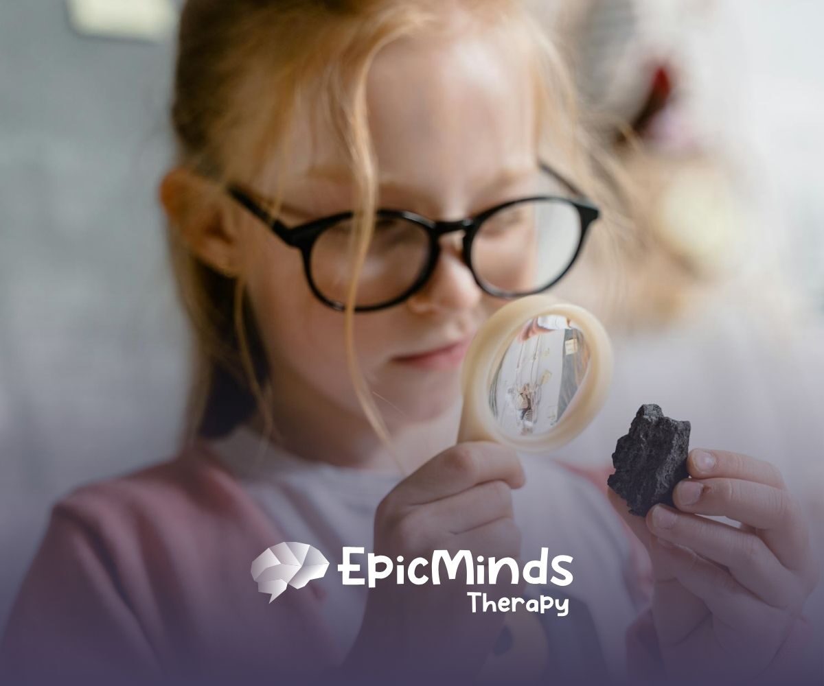 An autistic girl with glasses examining a rock closely through a magnifying glass during ABA therapy in North Carolina.