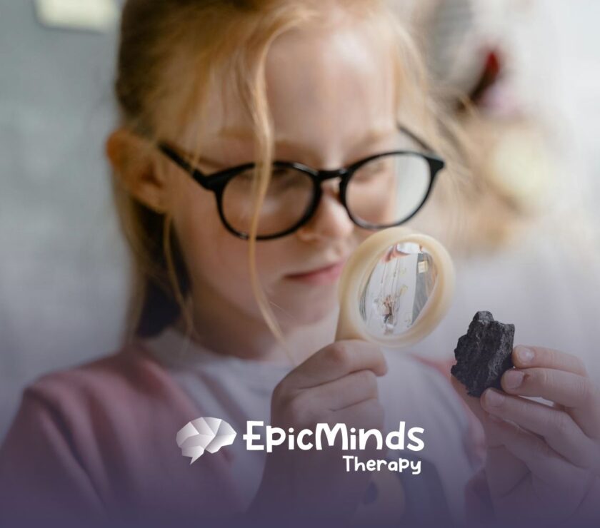 An autistic girl with glasses examining a rock closely through a magnifying glass during ABA therapy in North Carolina.