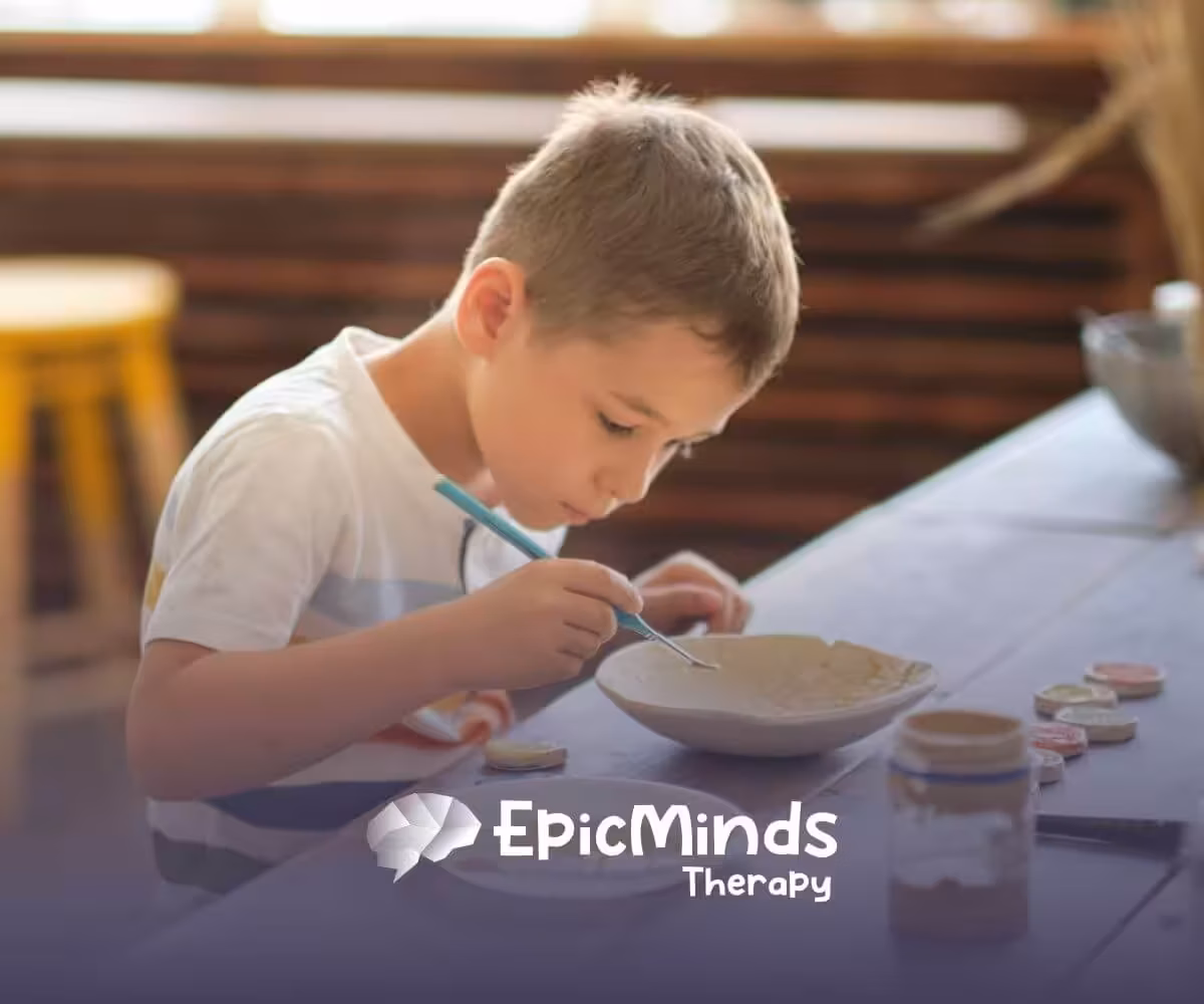 A child with autism painting a ceramic bowl at a wooden table.
