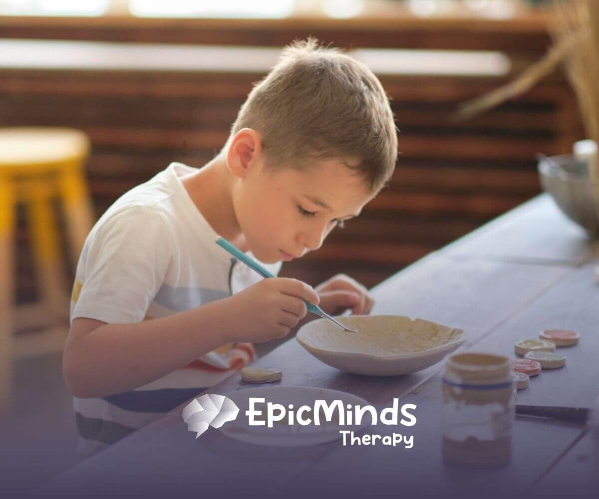A child with autism painting a ceramic bowl at a wooden table.