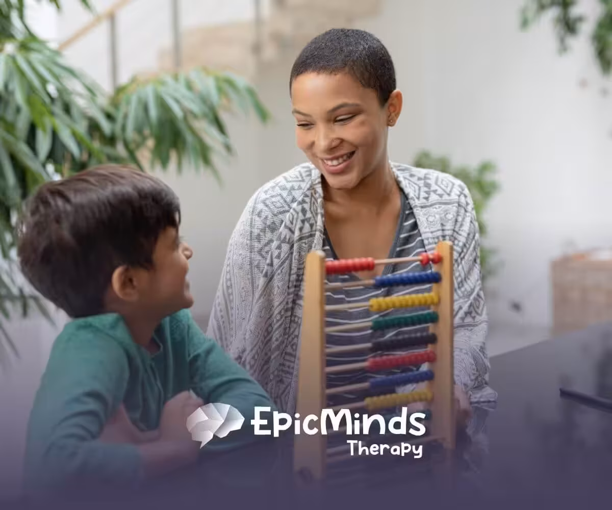 Smiling BCBA teaching young boy with an abacus in ABA therapy.