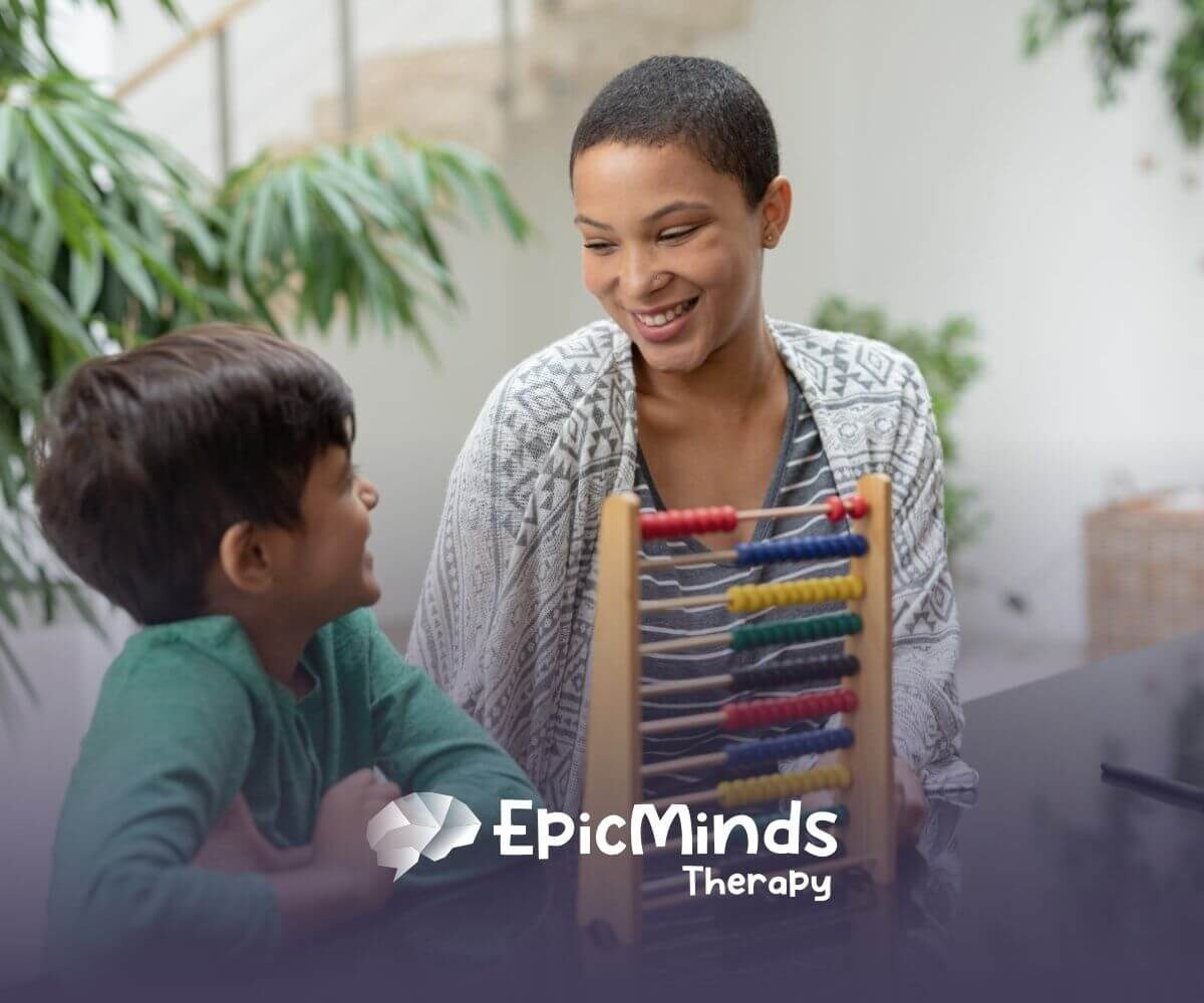 Smiling BCBA teaching young boy with an abacus in ABA therapy.