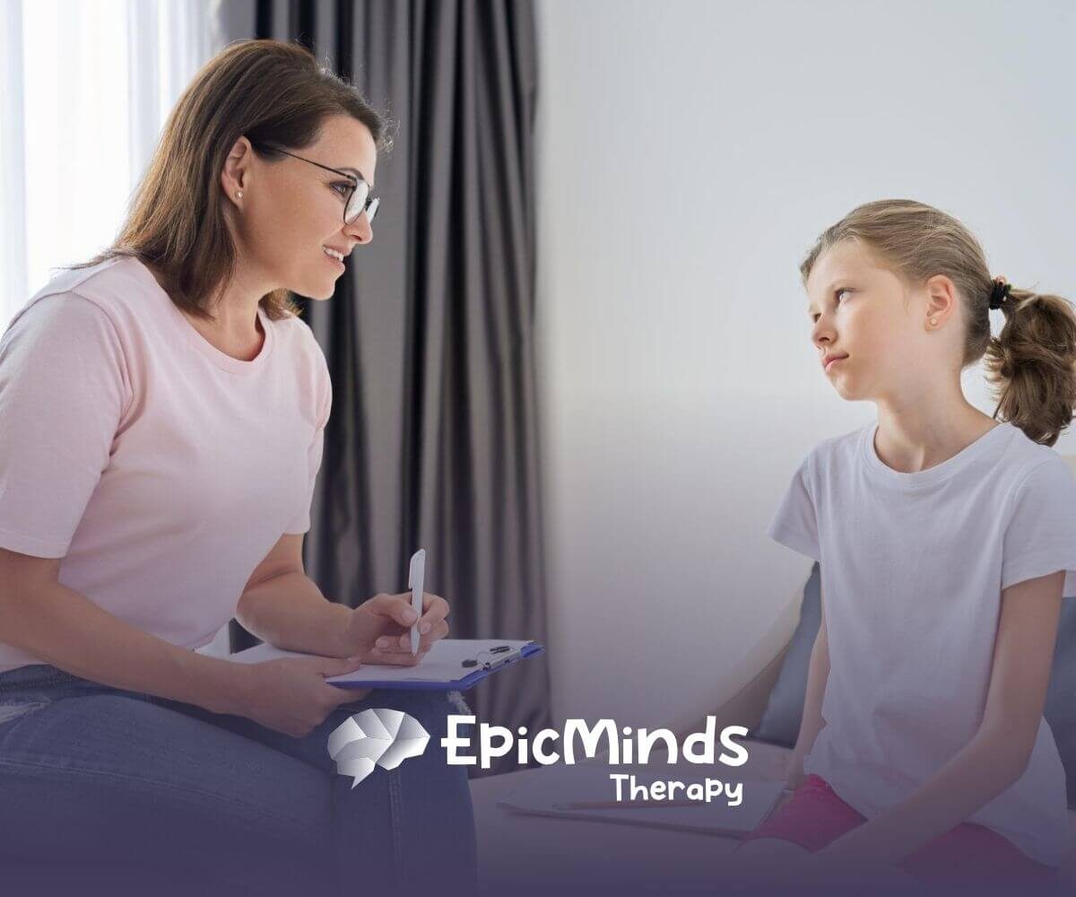 A female BCBA talking to a young girl with autism holding a clipboard in ABA therapy.