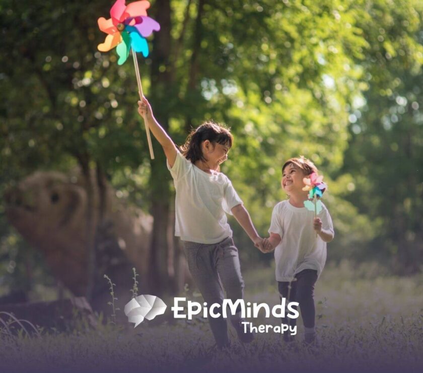 Two children with autism holding hands and playing with pinwheels outdoors.