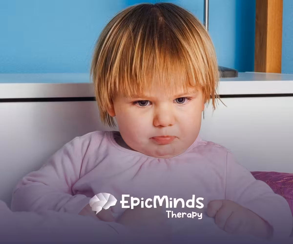 An autistic toddler in pink pajamas looking upset with a pouty expression during ABA therapy session in NC.