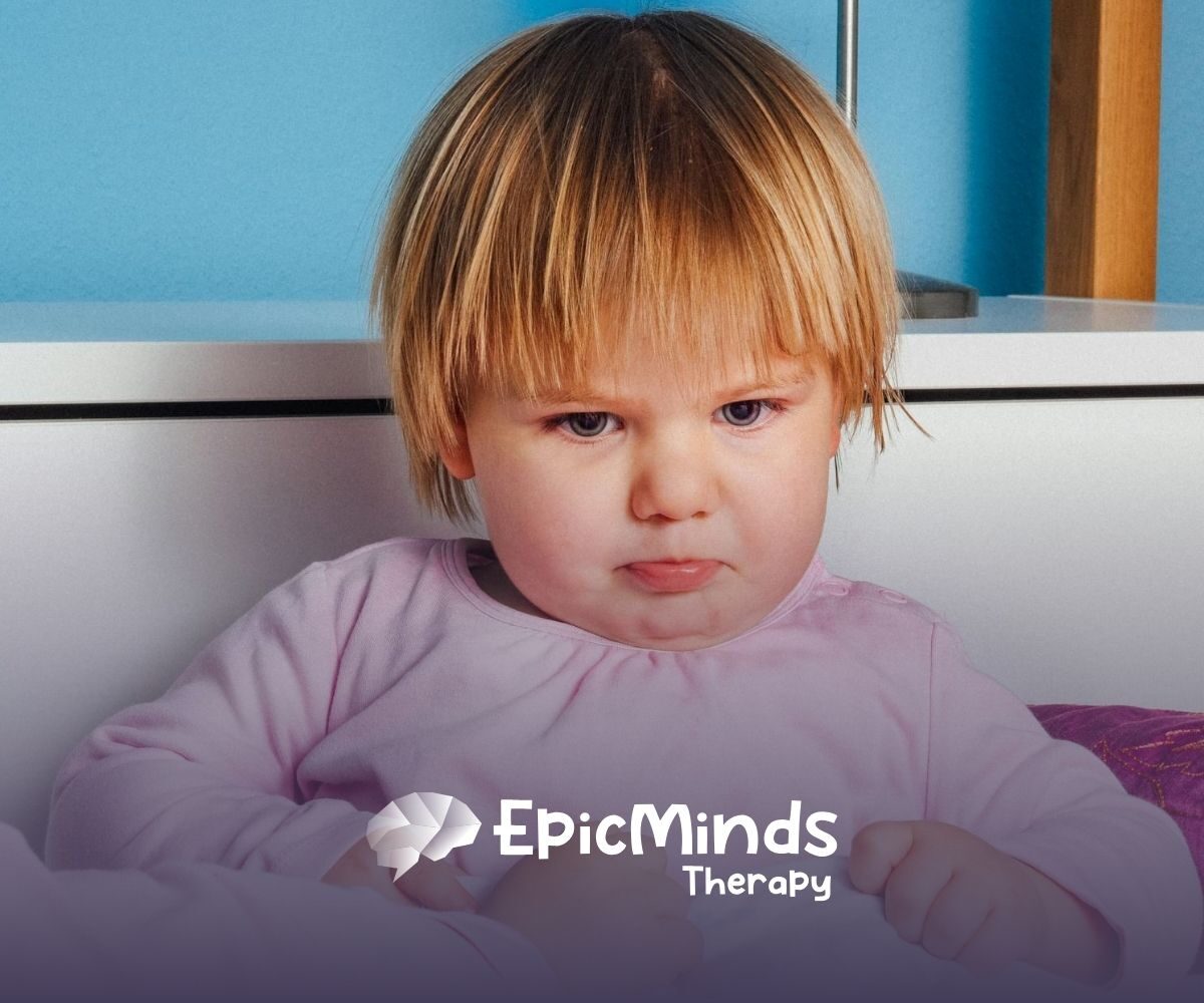 An autistic toddler in pink pajamas looking upset with a pouty expression during ABA therapy session in NC.