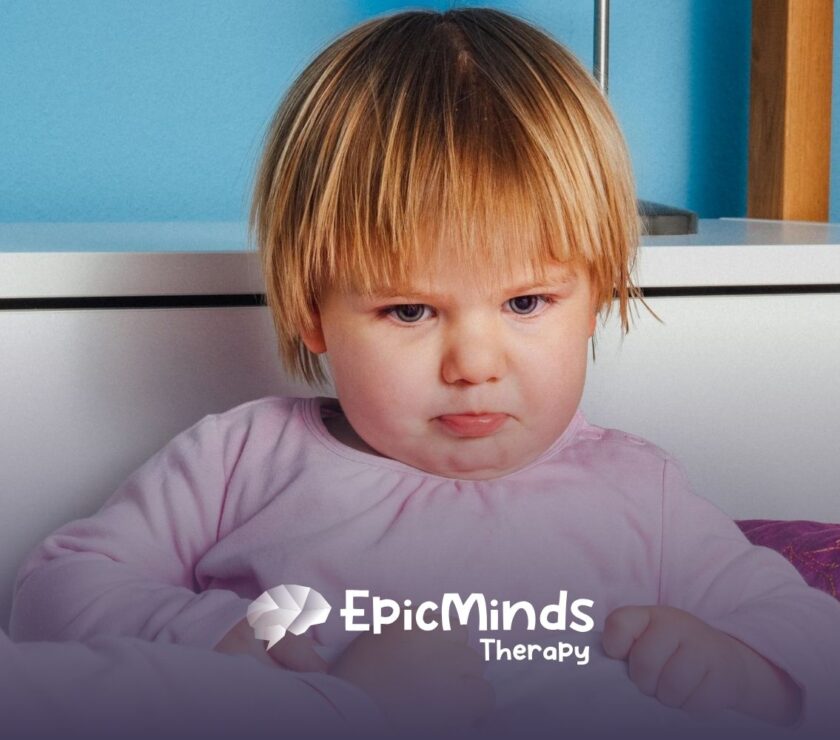 An autistic toddler in pink pajamas looking upset with a pouty expression during ABA therapy session in NC.