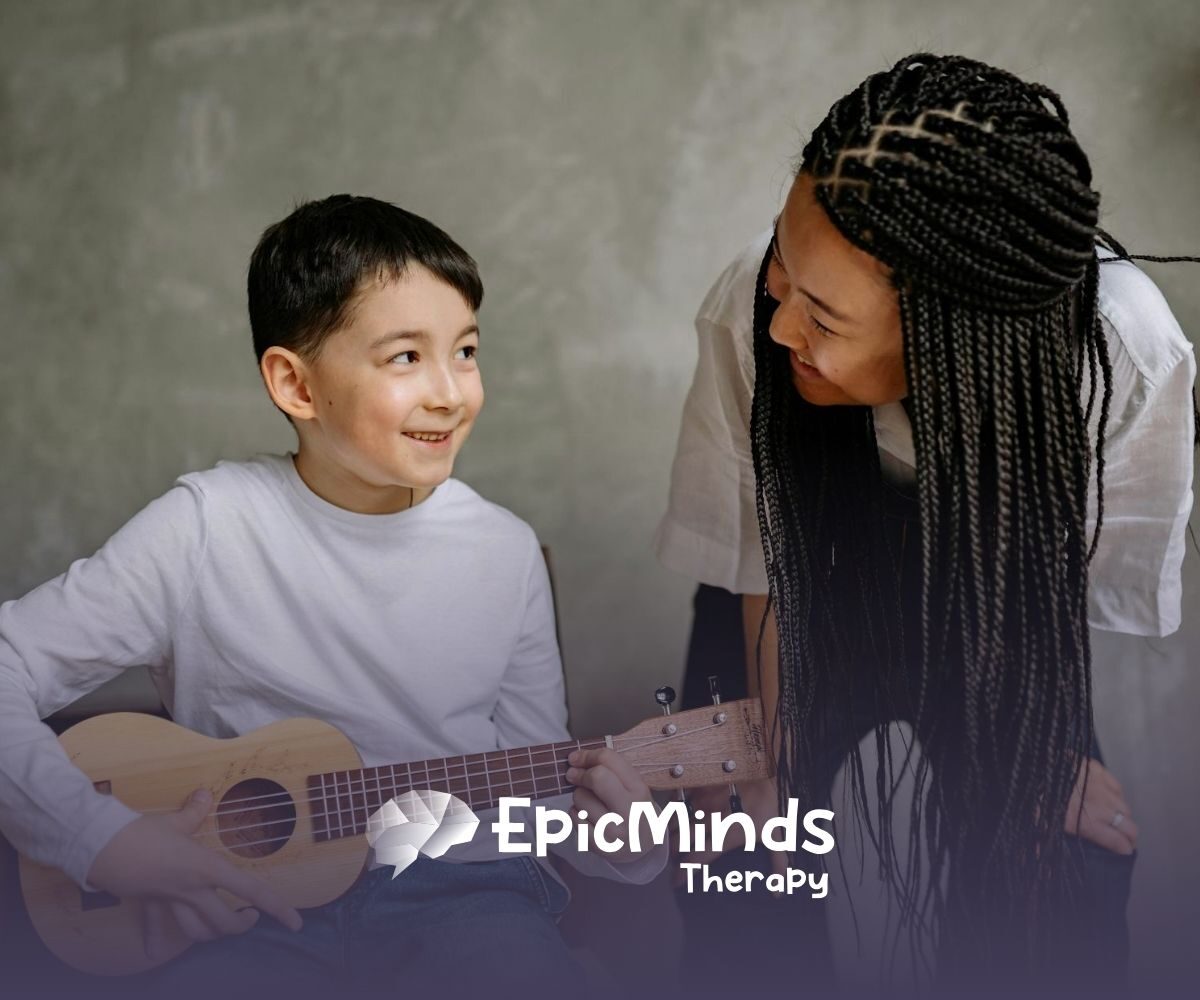 An autistic boy smiling while playing a small guitar as an RBT with braids leans toward him during ABA therapy in NC.