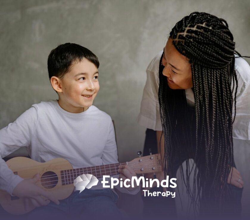An autistic boy smiling while playing a small guitar as an RBT with braids leans toward him during ABA therapy in NC.