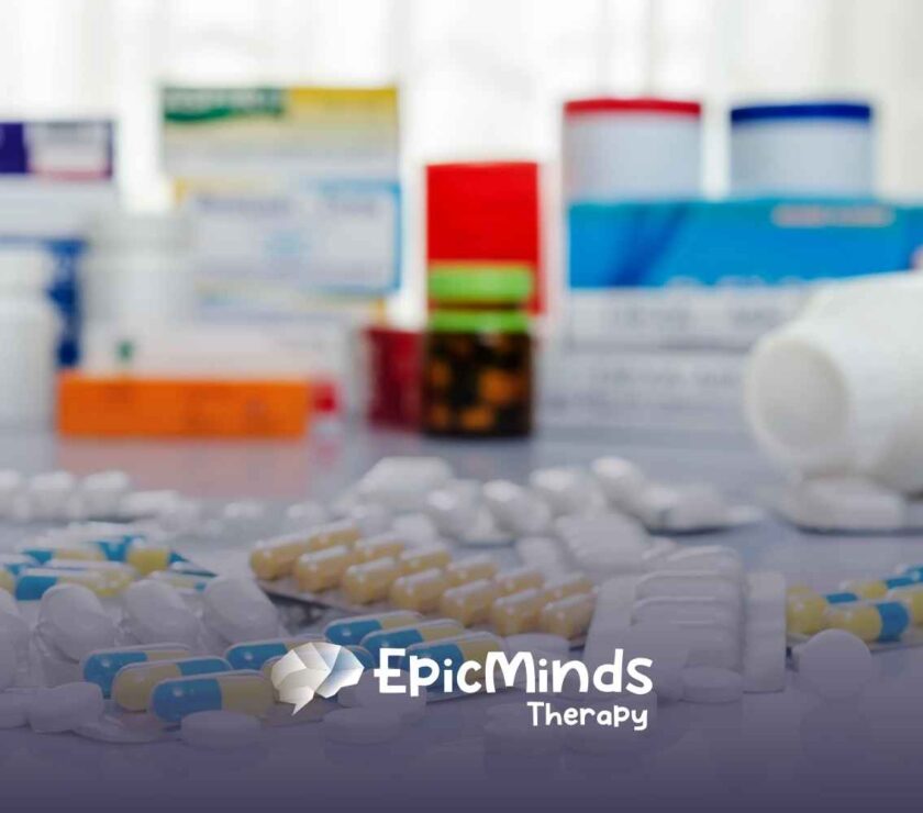 A variety of pills and capsules are scattered on a white surface, with medicine boxes blurred in the background. The image conveys a clinical or pharmaceutical setting.