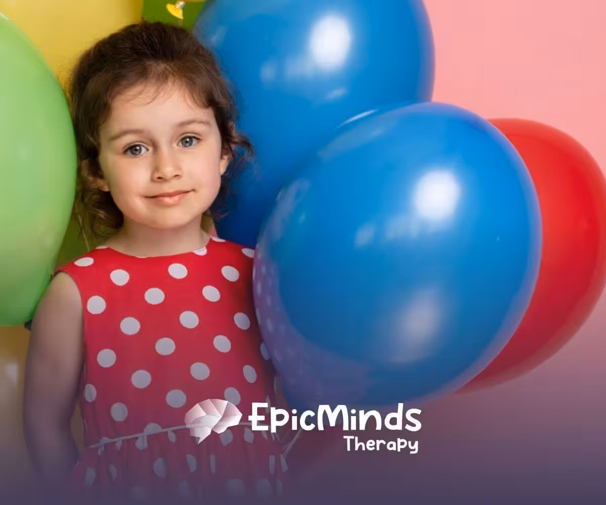 Smiling girl with autism in a red polka-dot dress standing with colorful balloons.