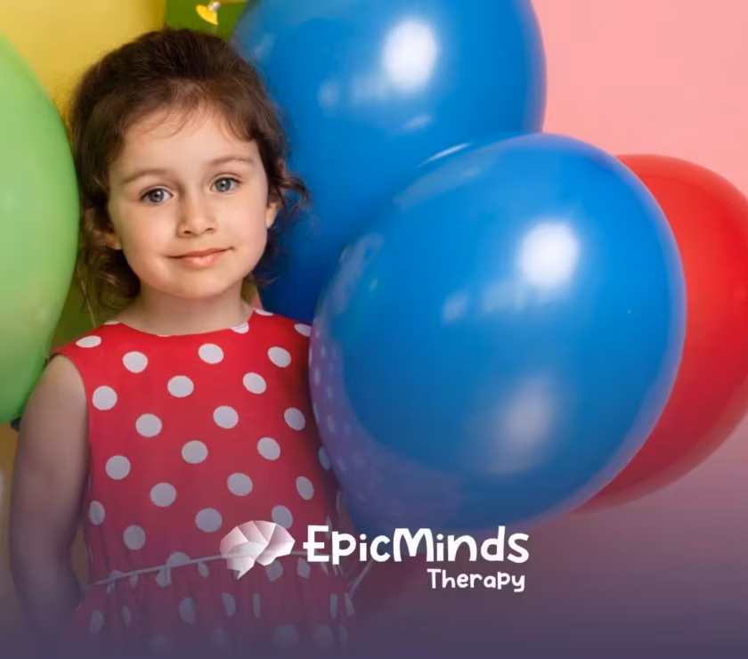 Smiling girl with autism in a red polka-dot dress standing with colorful balloons.