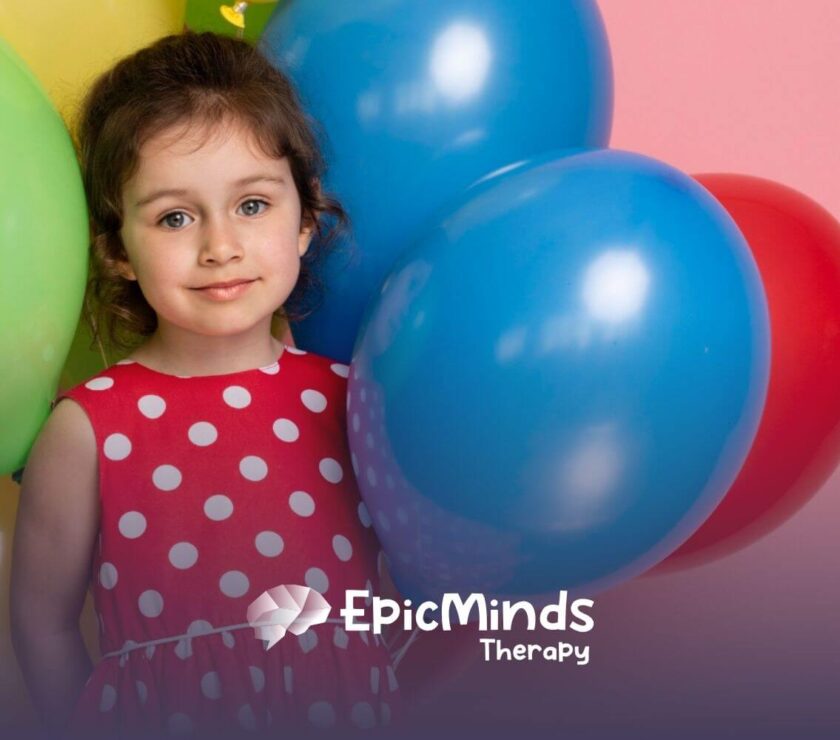 Smiling girl with autism in a red polka-dot dress standing with colorful balloons.