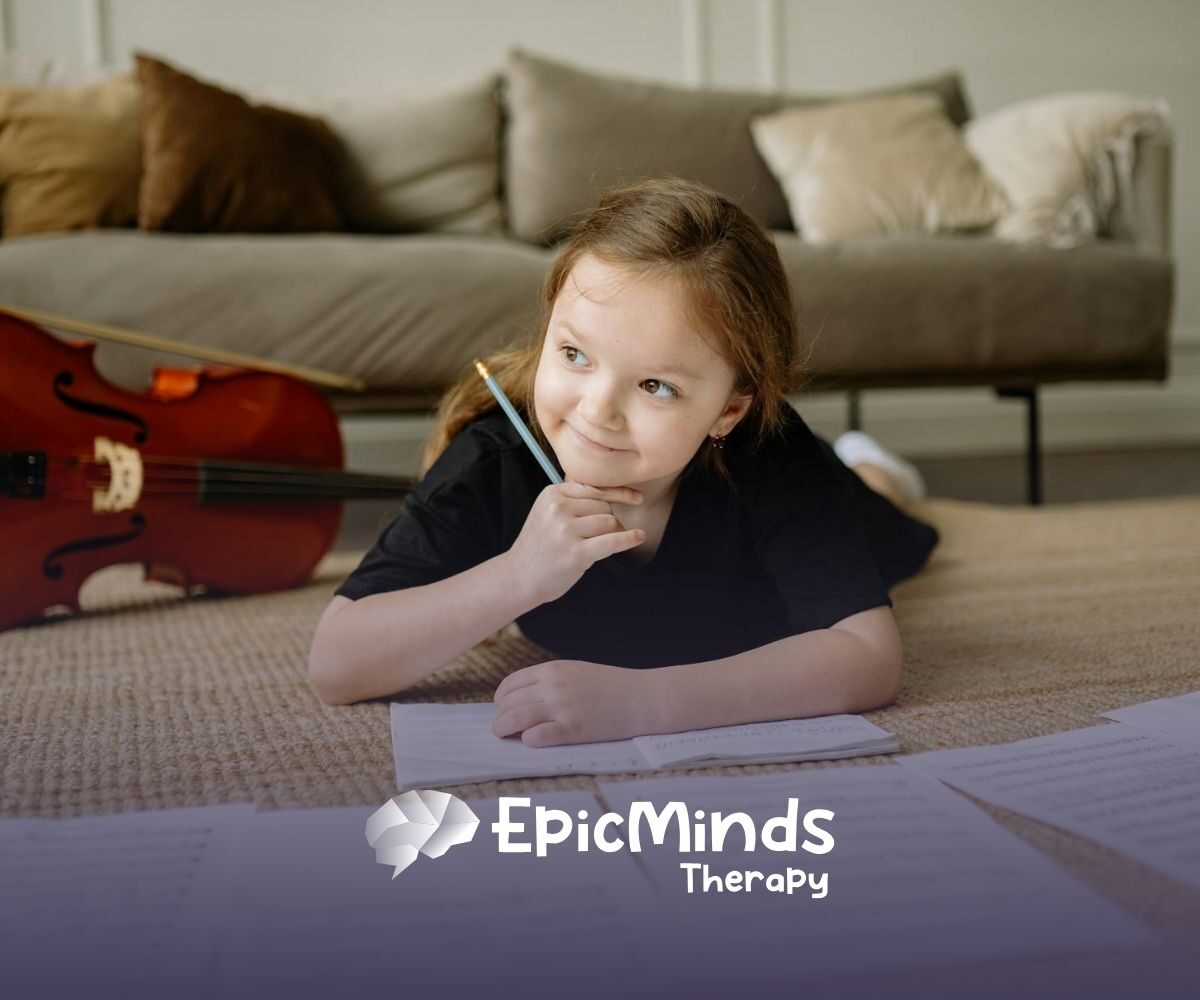 An autistic girl lying on the floor, smiling while writing music notes beside a cello during ABA therapy in NC.