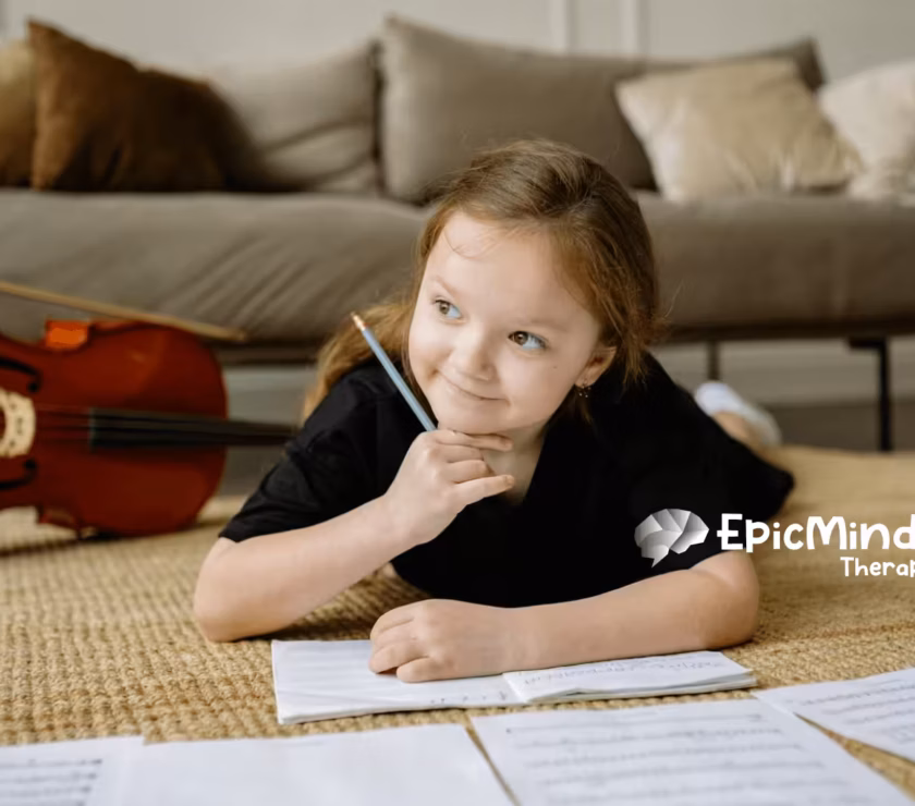 An autistic girl lying on the floor, smiling while writing music notes beside a cello during ABA therapy in NC.