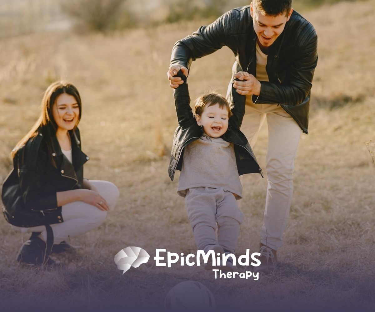 Mom and dad kick a ball with their giggling child in a grassy field on a sunny afternoon in North Carolina.