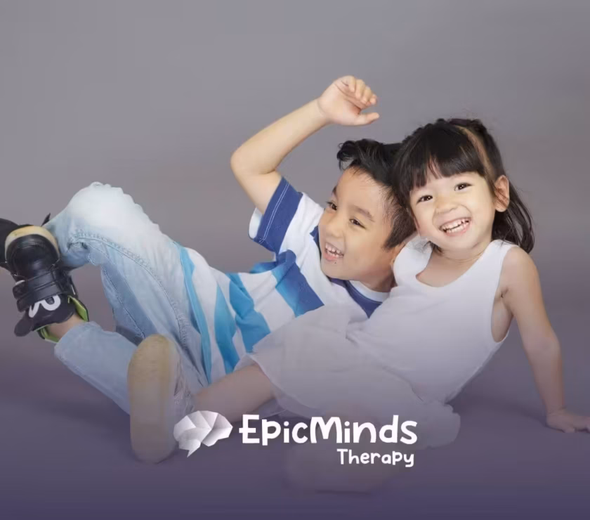 Two autistic boy and girl smiling while sitting on the floor posing playfully after their ABA Therapy.