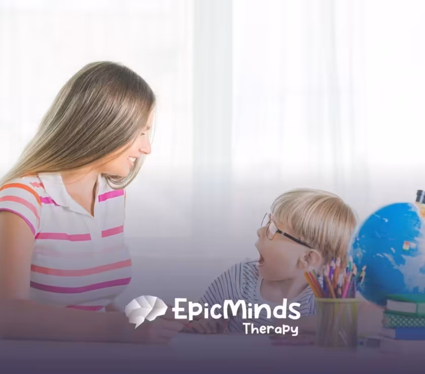 Therapist smiling and engaging with young boy during ABA therapy activity.