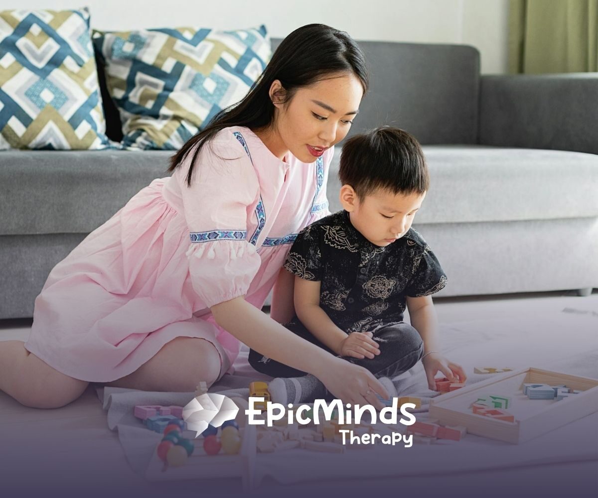 ABA therapist and young autistic kid are playing with wooden educational toys on the floor during ABA therapy in NC.