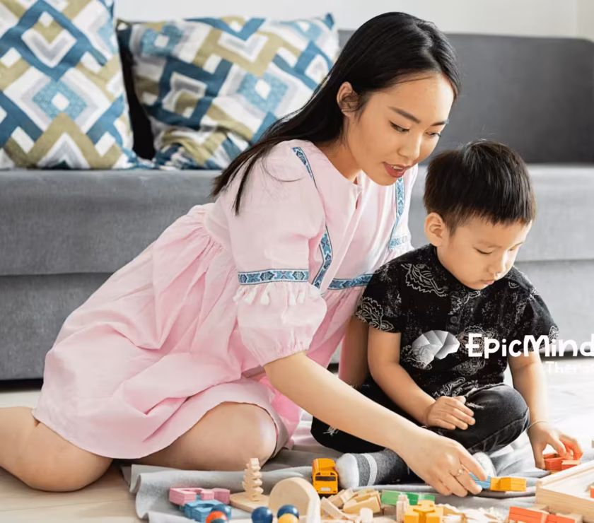ABA therapist and young autistic kid are playing with wooden educational toys on the floor during ABA therapy in NC.