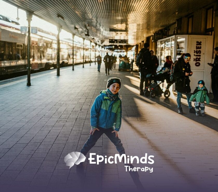 Smiling boy strikes a playful pose on a busy train platform filled with travelers and sunlight in North Carolina.