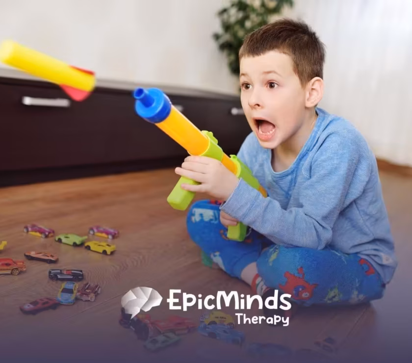 Young boy with autism sitting on the floor excitedly playing with a toy blaster and toy cars.