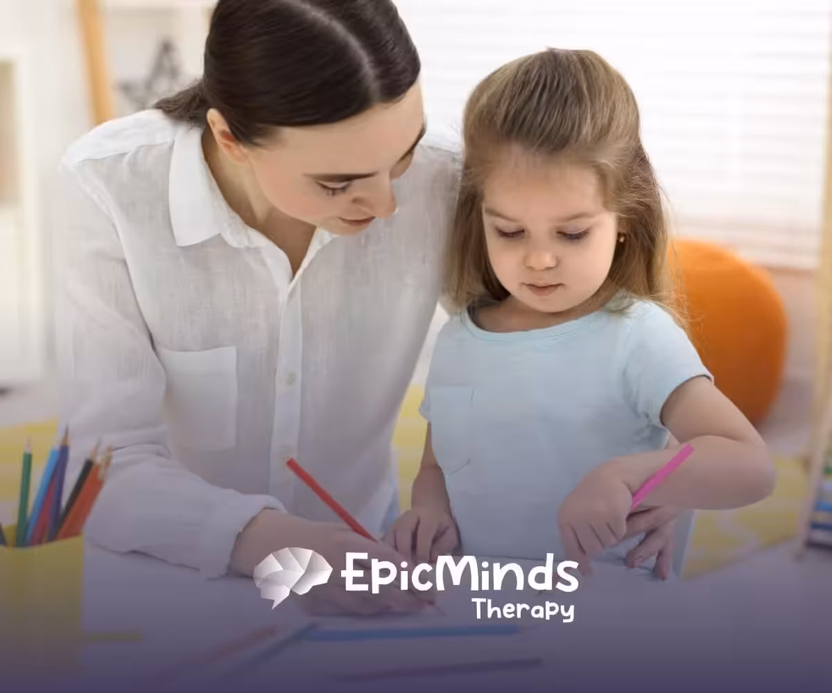 Therapist helping young girl draw with colored pencils at a table during ABA therapy.
