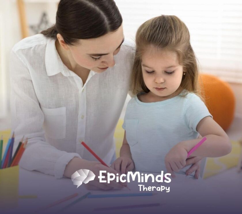 Therapist helping young girl draw with colored pencils at a table during ABA therapy.