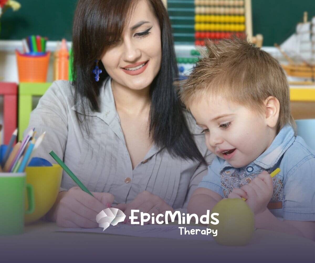 Therapist smiling and drawing with young child during ABA therapy session.