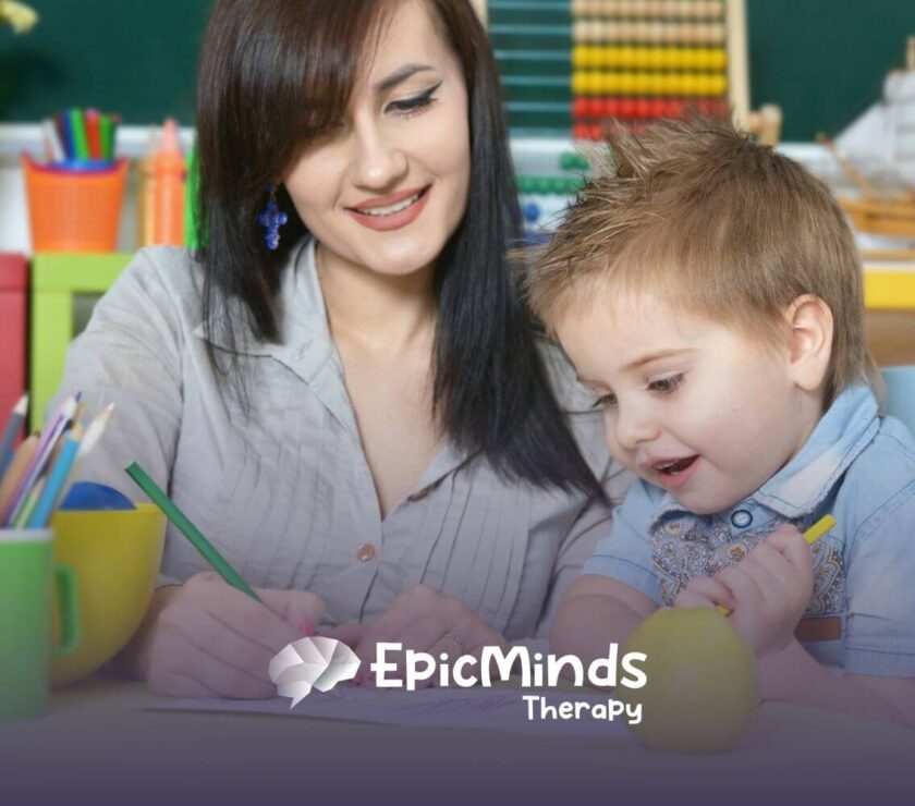 Therapist smiling and drawing with young child during ABA therapy session.