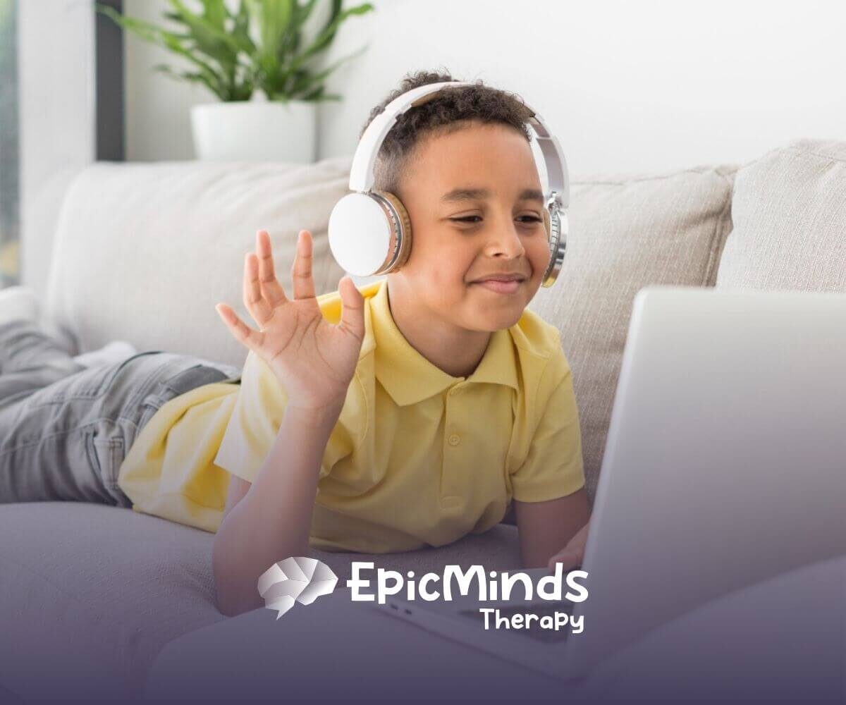 Child with autism wearing headphones waving at laptop while lying on a couch