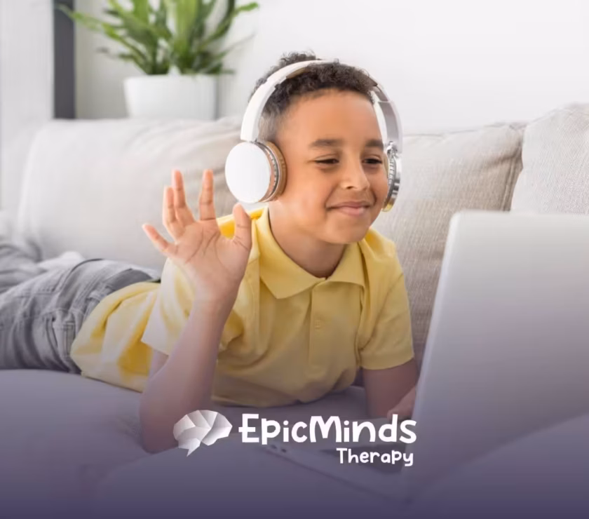 Child with autism wearing headphones waving at laptop while lying on a couch