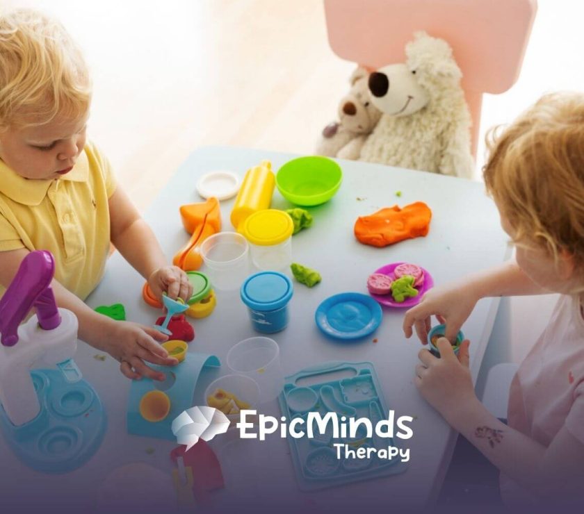 Two children with autism playing with colorful playdough and plastic tools on a table.