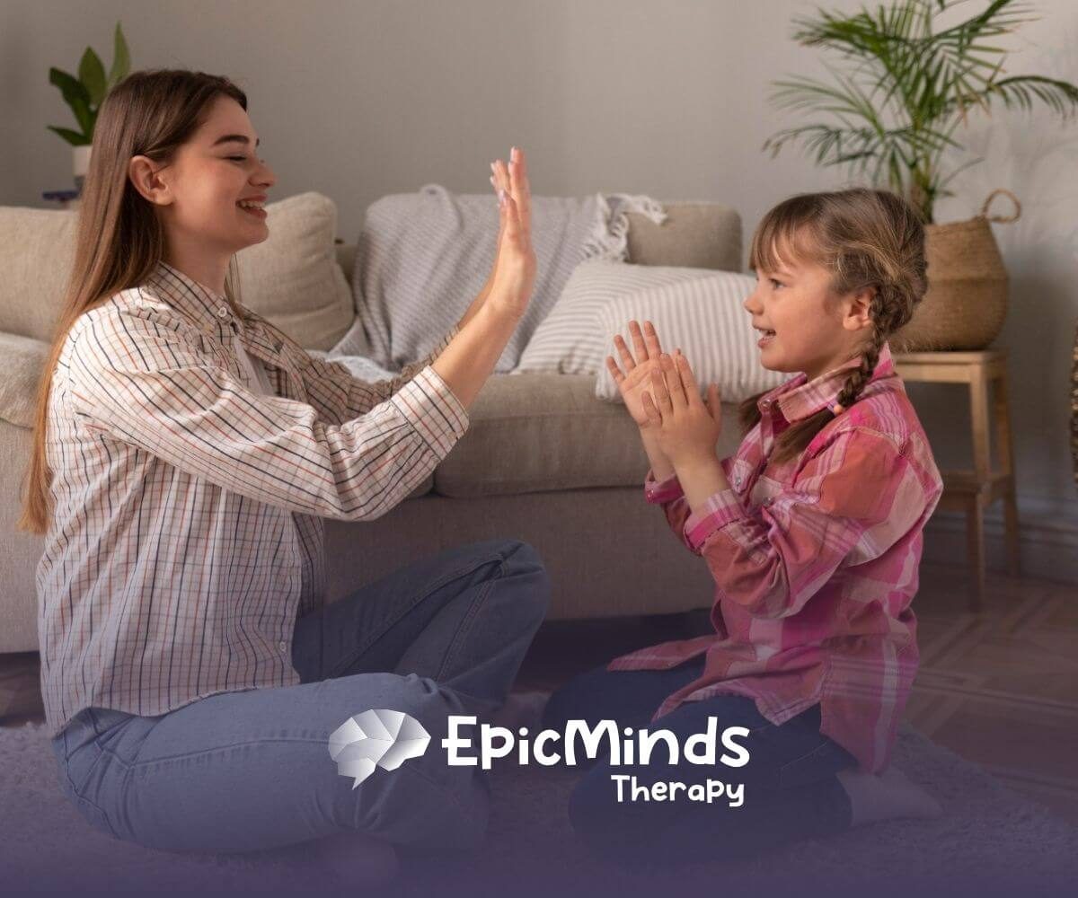 A BCBA and a girl with autism playing a hand-clapping game indoors during ABA therapy activity.