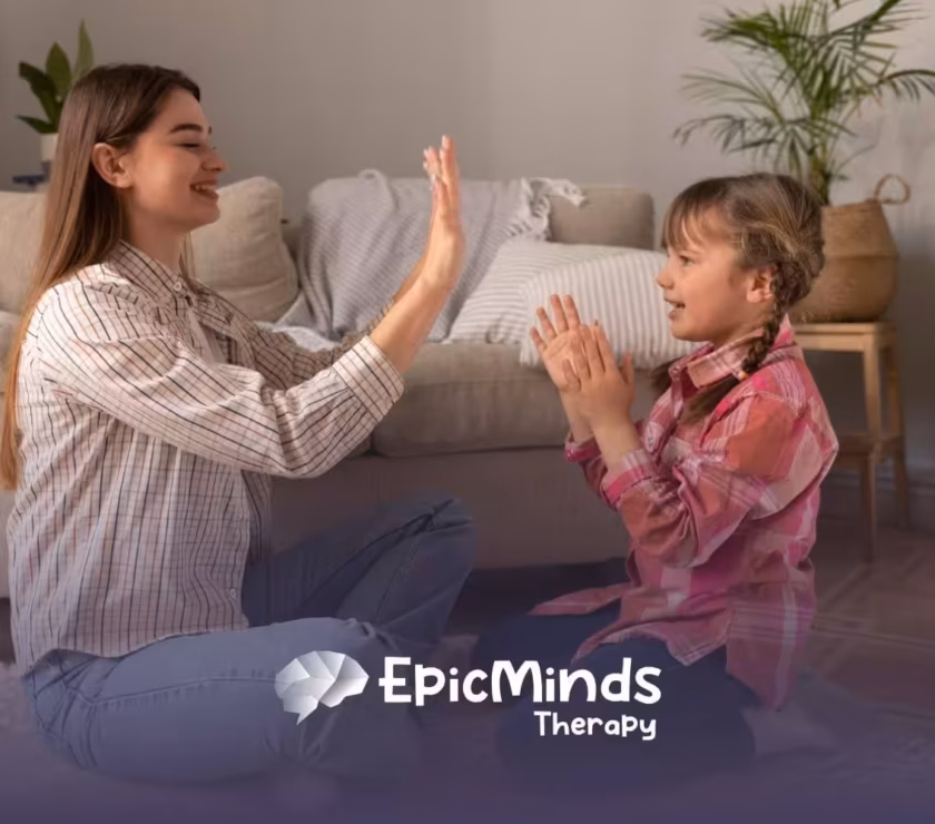 A BCBA and a girl with autism playing a hand-clapping game indoors during ABA therapy activity.