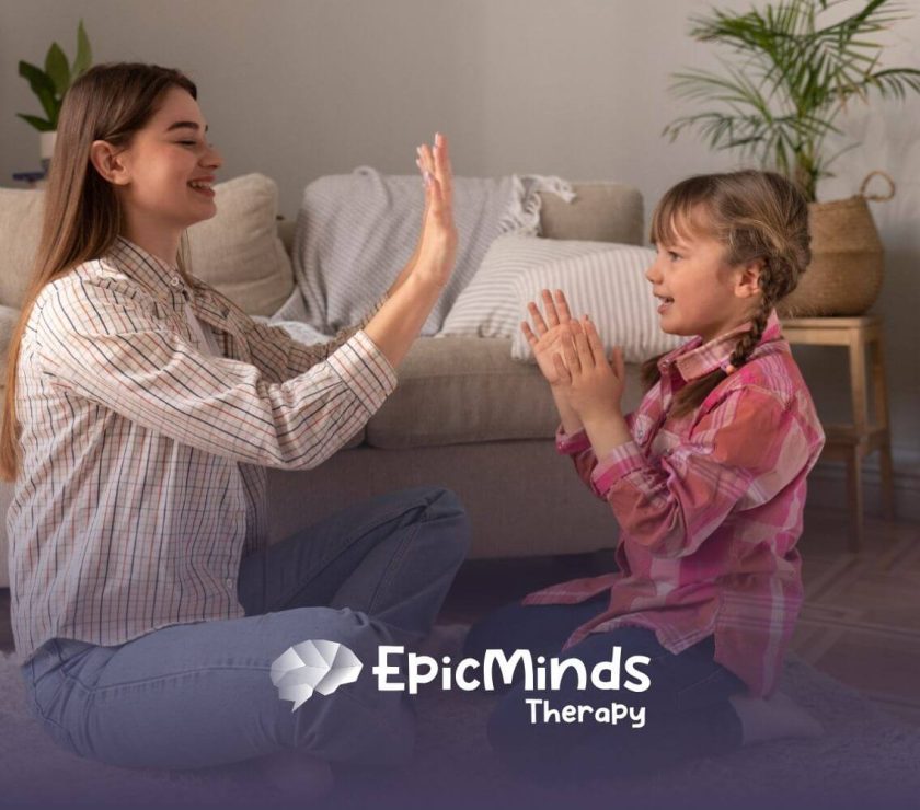 A BCBA and a girl with autism playing a hand-clapping game indoors during ABA therapy activity.
