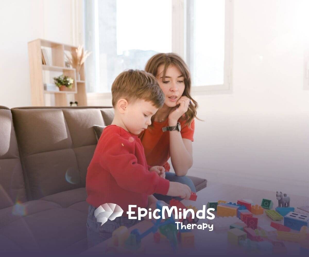 A young boy with autism building with colorful blocks while a BCBA watches beside him during ABA therapy.