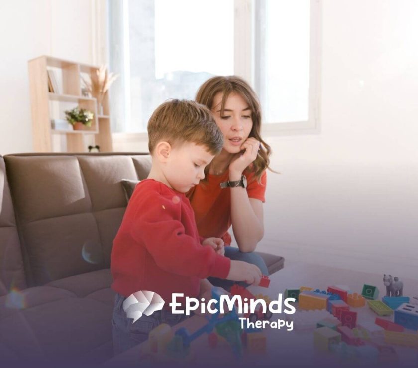 A young boy with autism building with colorful blocks while a BCBA watches beside him during ABA therapy.
