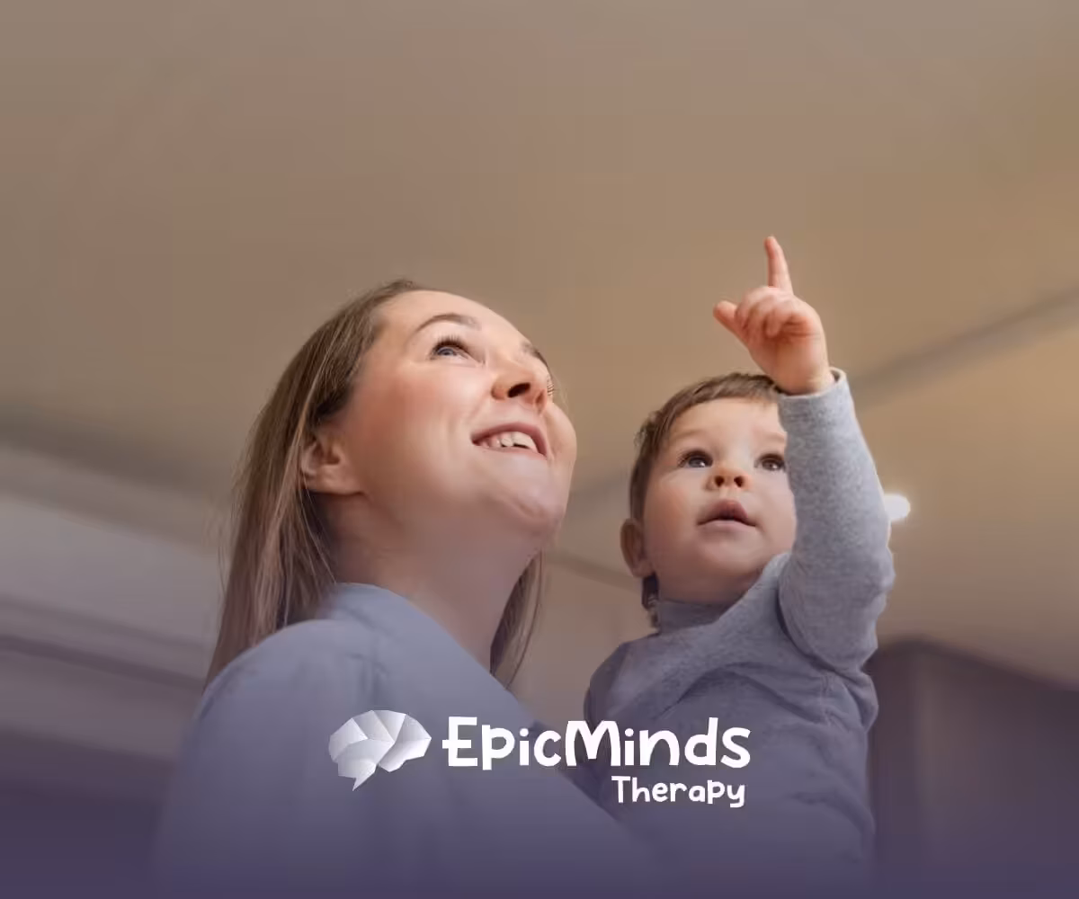 A BCBA holding a young child with autism while the child points upward.