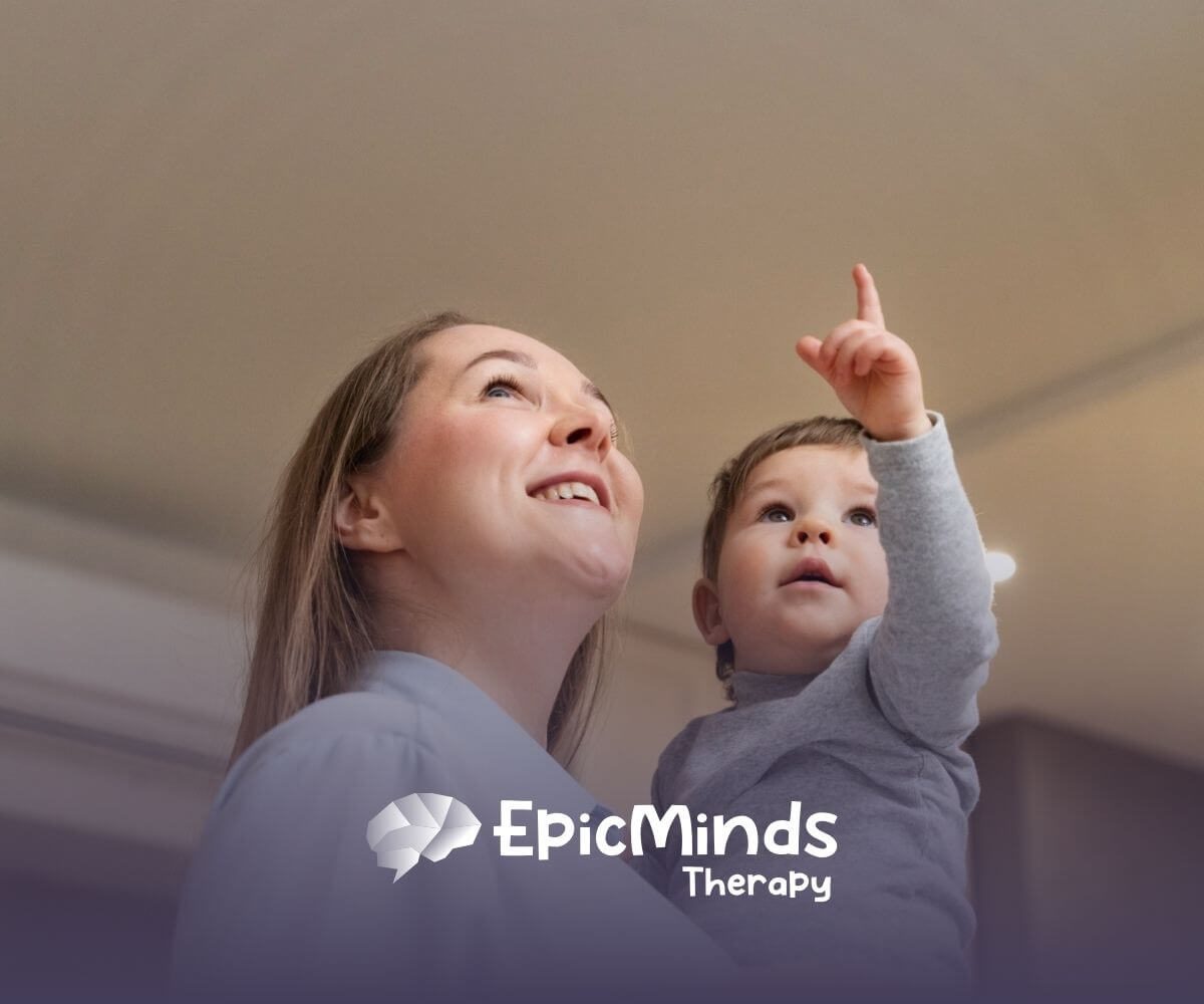 A BCBA holding a young child with autism while the child points upward.