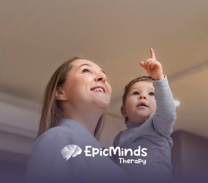 A BCBA holding a young child with autism while the child points upward.