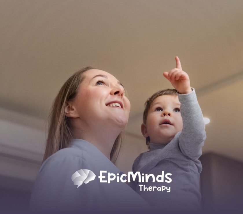 A BCBA holding a young child with autism while the child points upward.