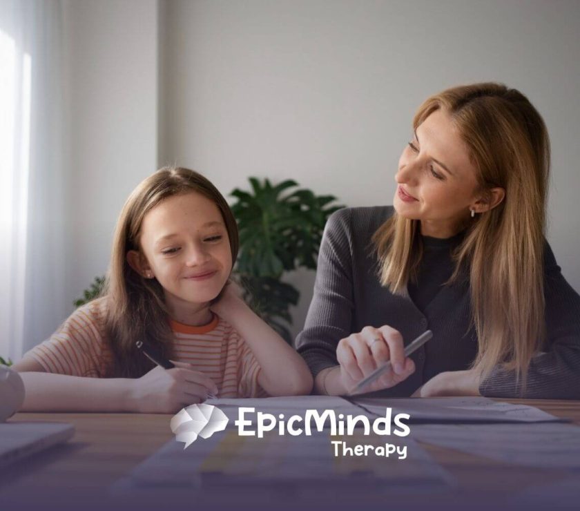 A BCBA and girl with autism sitting at a desk during ABA therapy session.