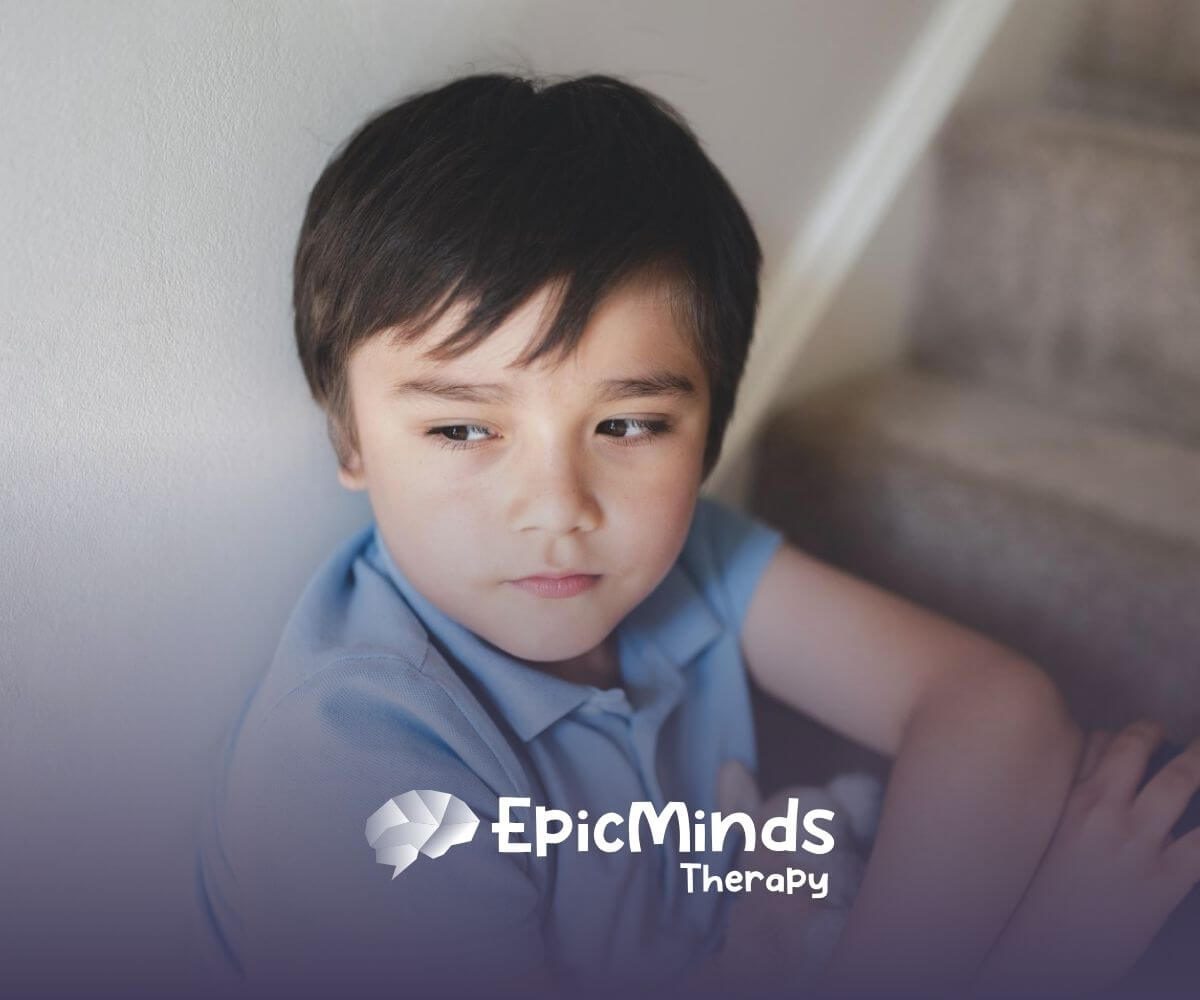 A boy with severe autism sitting on stairs, looking pensive with a stuffed animal in his lap.