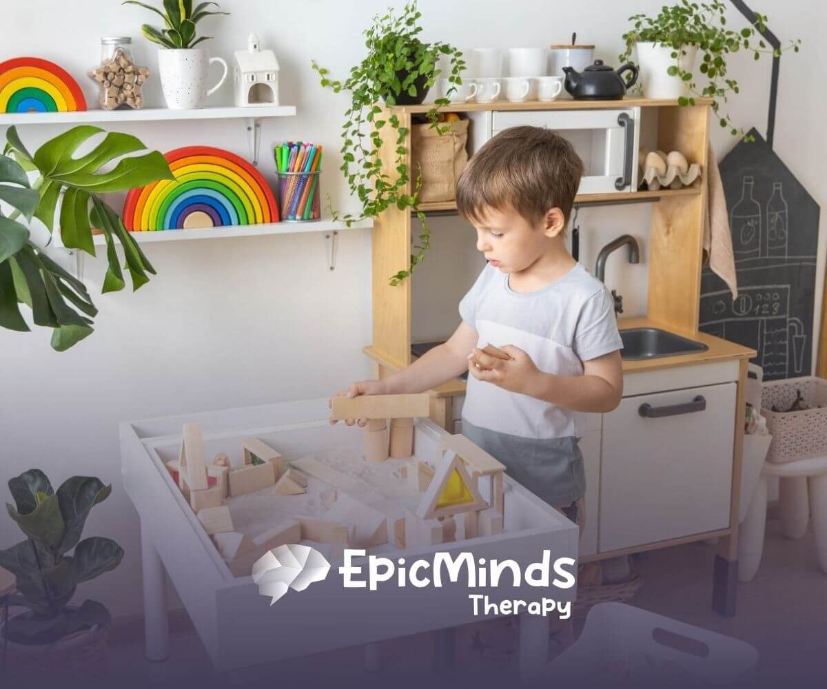 A young boy with autism playing with wooden blocks on a table in a brightly decorated playroom.