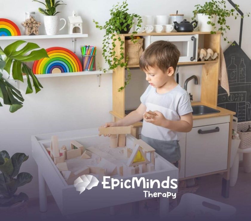 A young boy with autism playing with wooden blocks on a table in a brightly decorated playroom.