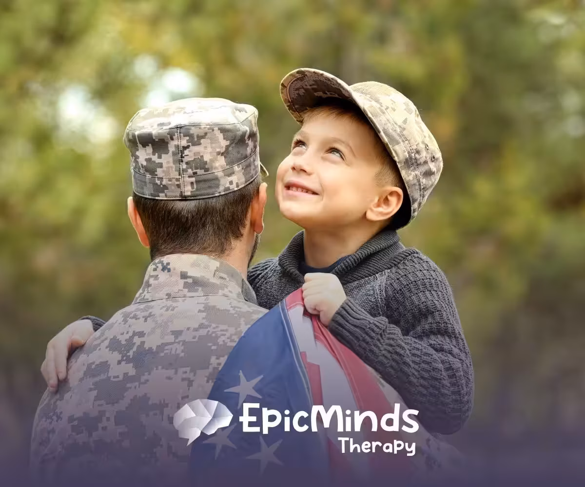 A joyful child wrapped in a U.S. flag smiles up at a person in military camouflage holding them. The background is a blurred green outdoors.