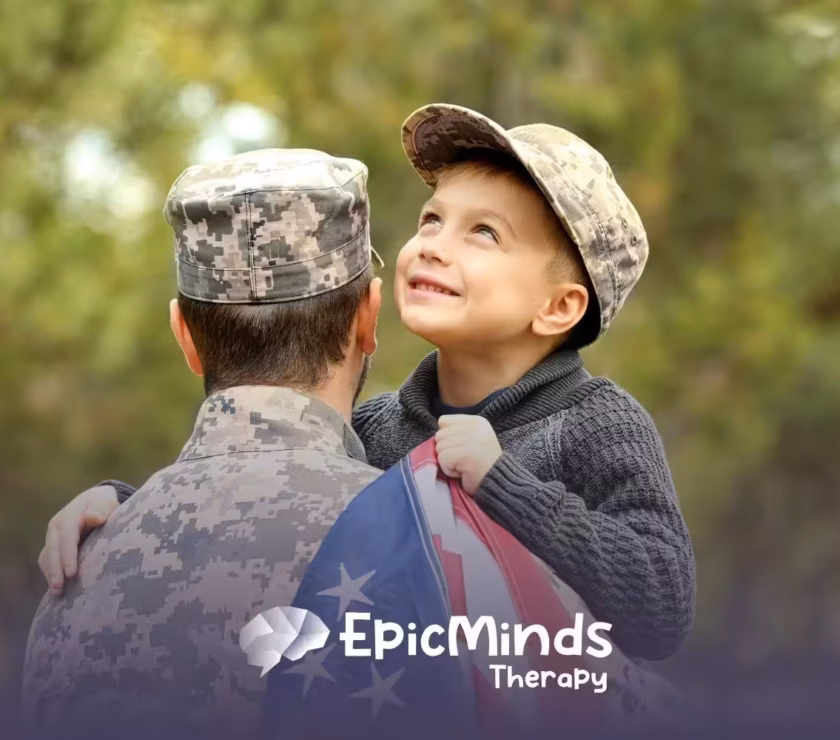 A joyful child wrapped in a U.S. flag smiles up at a person in military camouflage holding them. The background is a blurred green outdoors.